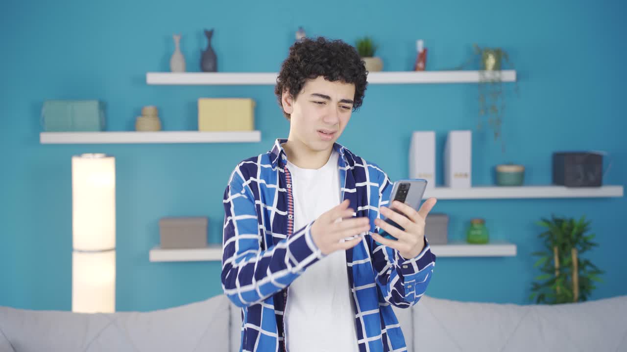 십대 남성이 집에서 스마트폰으로 소셜 미디어를 검색하고 있습니다.