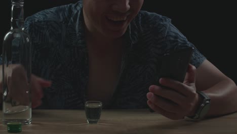 close up of asian man pouring vodka in a shot glass before drinking during having video call in black background