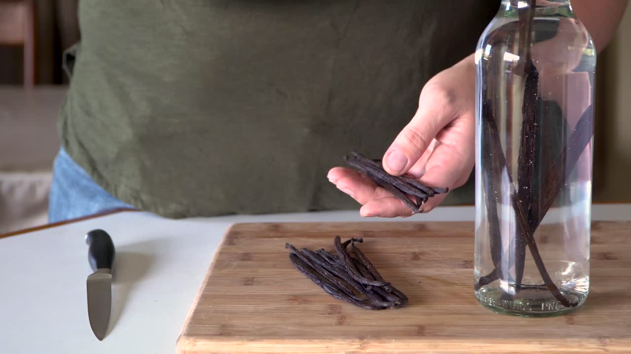 Woman drops vanilla beans into glass bottle of alcohol, vanilla extract
