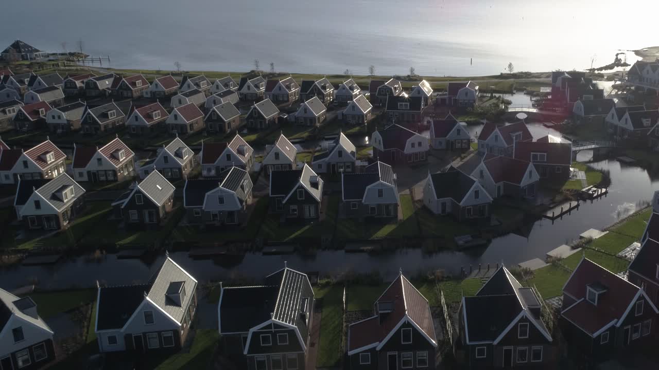 Luftfoto, der zoomer ud fra en lille hollandsk feriepark ved siden af havet under solnedgang med flotte lange skygger