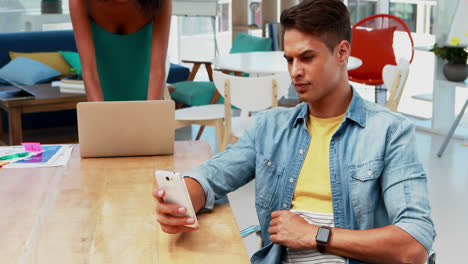 Male-executive-using-mobile-phone-while-colleague-using-laptop-4k