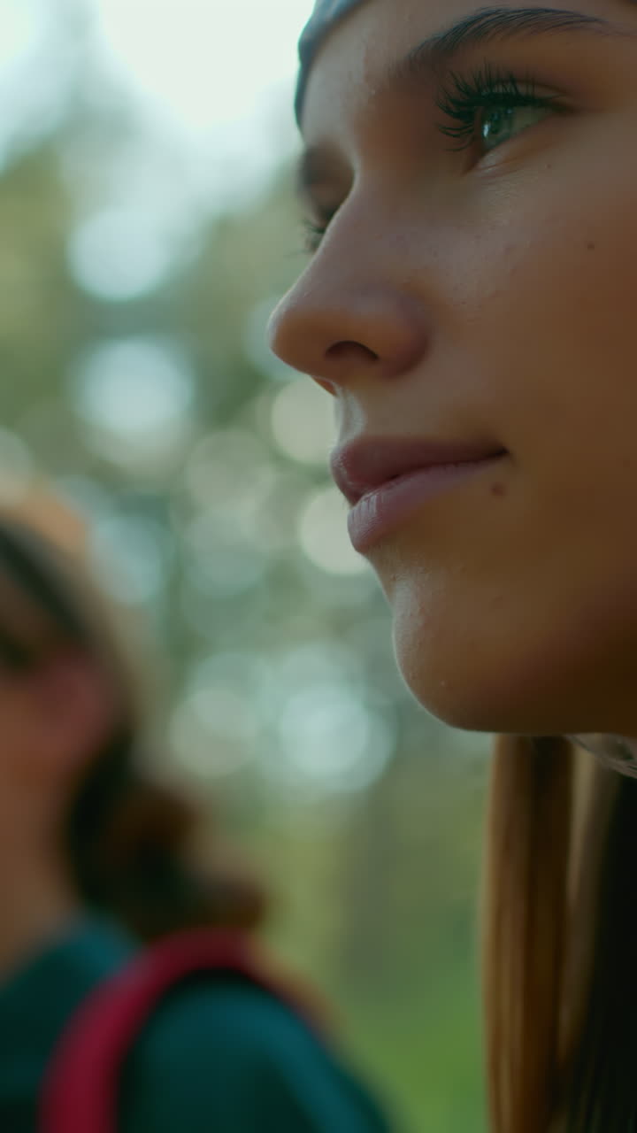 primer plano de hermanas caminando a través de un bosque verde exuberante, una con una bufanda azul, iluminada por la luz del sol que se refleja en su cabello mientras mira a su alrededor, efecto borroso suave en el compañero