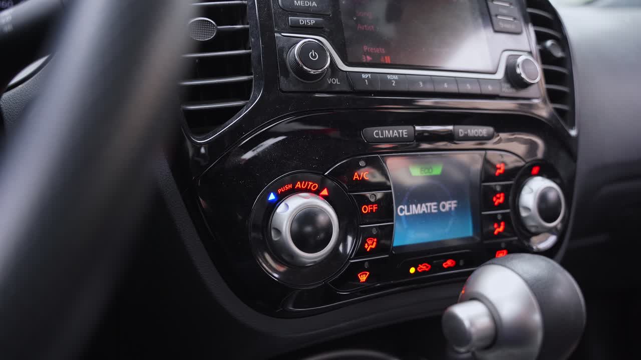 Una console centrale di un veicolo dotata di uno schermo digitale per il controllo del clima e di un sistema di infotainment. Il display mostra le impostazioni Clima Spento e modalità Eco in un elegante interno nero.