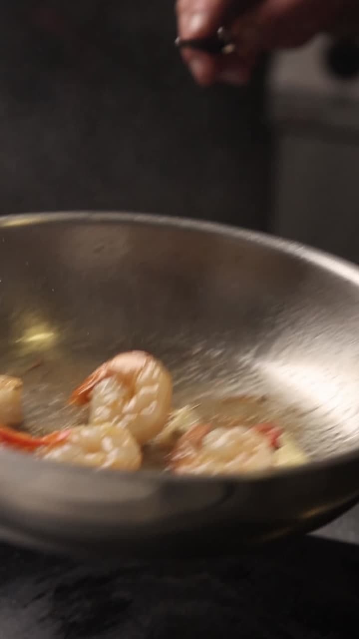 Chef che frigge gamberetti con aglio e peperoncino in una padella calda