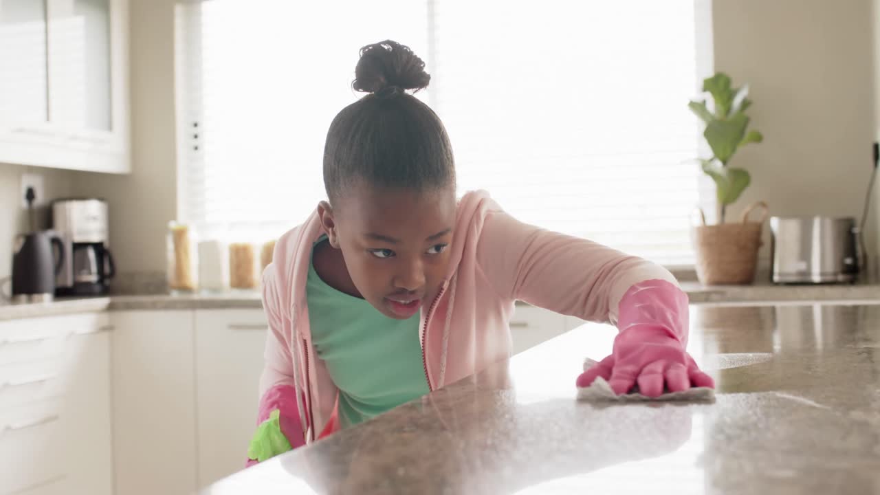 Happy african american girl cleaning countertop in kitchen, in slow motion