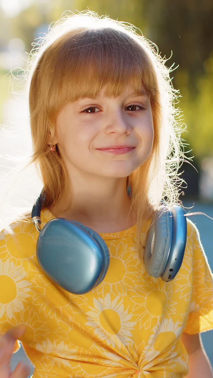 Bambina felice con le cuffie wireless che sceglie di ascoltare musica nello smartphone che balla all'aperto