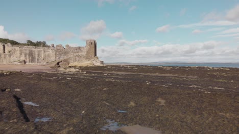 Vista-Aérea-De-Drones-Acercándose-Al-Castillo-De-St-Andrews,-Volando-Muy-Bajo-Al-Suelo-Rocoso-Que-Rodea-La-Bahía-De-St-Andrews-En-Escocia,-Reino-Unido