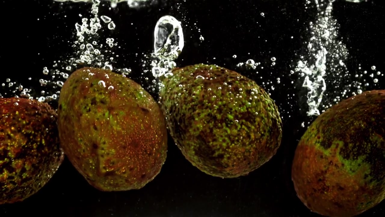 Avocado freschi che schizzano nell'acqua al rallentatore su sfondo nero