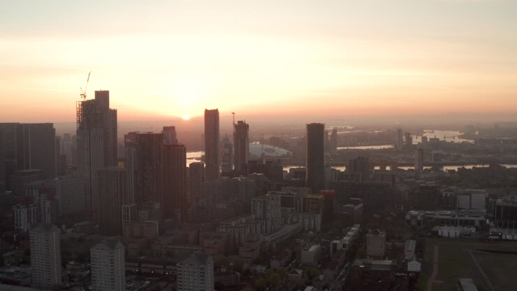 Plano aéreo deslizante de grandes arranha-céus a pequenos edifícios residenciais, nascer do sol em Canary Wharf