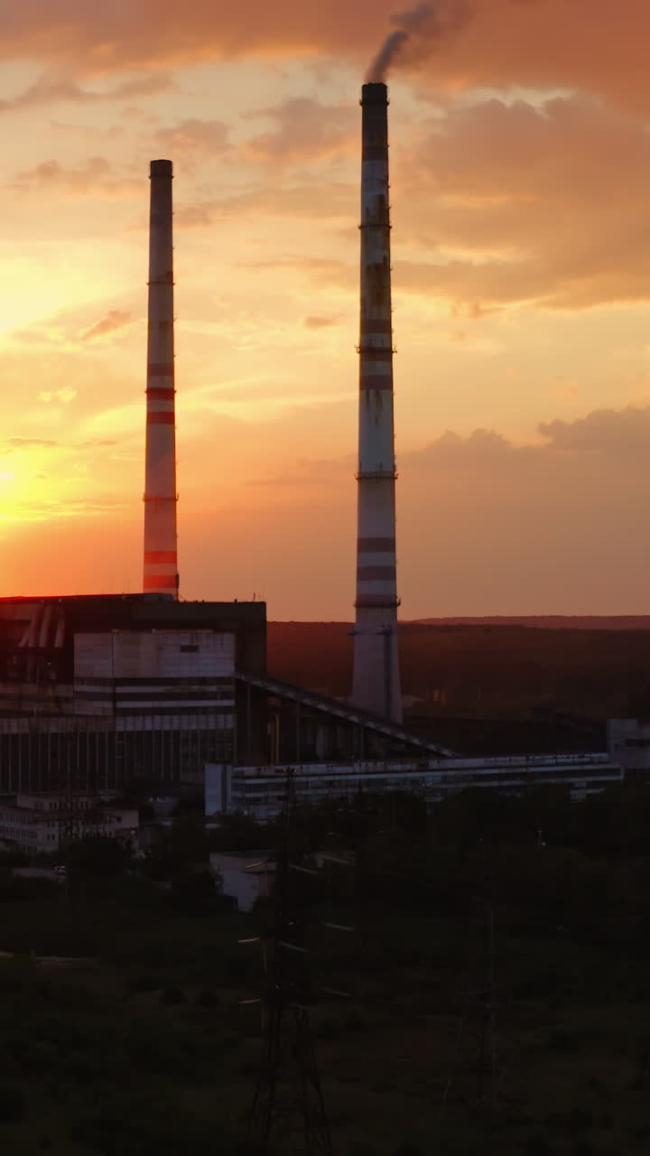 Factory in the evening. Dirty emissions from industrial pipes filling the air at sunset. Ecological problems. Aerial view. Camera rising up. Vertical video