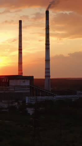 factory in the evening. dirty emissions from industrial pipes filling the air at sunset. ecological problems. aerial view. camera rising up. vertical video