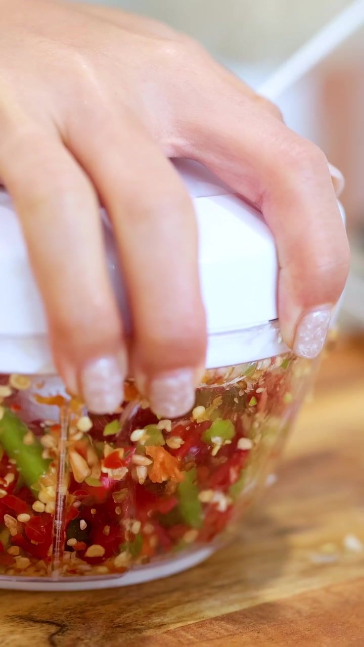 Hand operating a manual food processor to chop colorful vegetables on a wooden surface with natural lighting