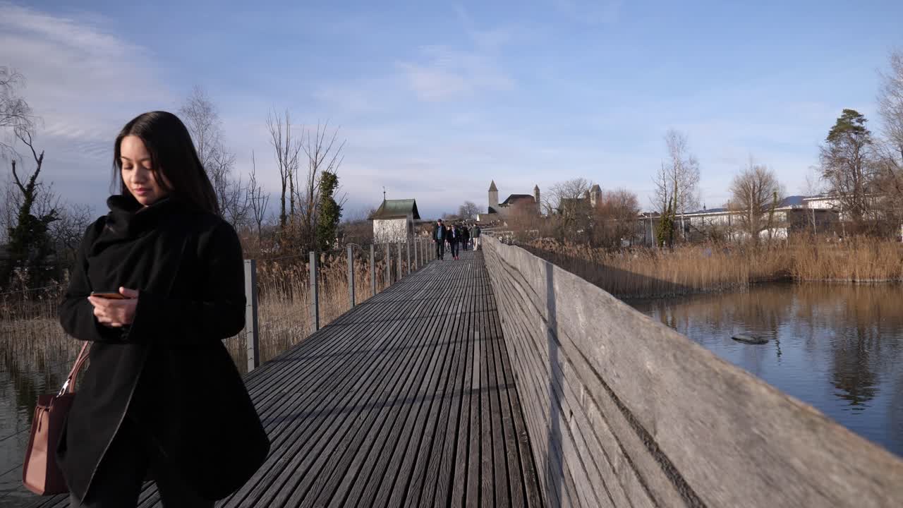 Rapperswil, İsviçre'de ahşap bir iskelede yürüyen ve telefonuna bakan genç bir Asyalı kadının sabit çekimi.