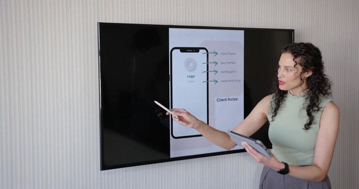 Donna afroamericana in movimento, con uno stilo bianco che appare, che tiene un tablet e spiega l'interfaccia utente del telefono in TV.