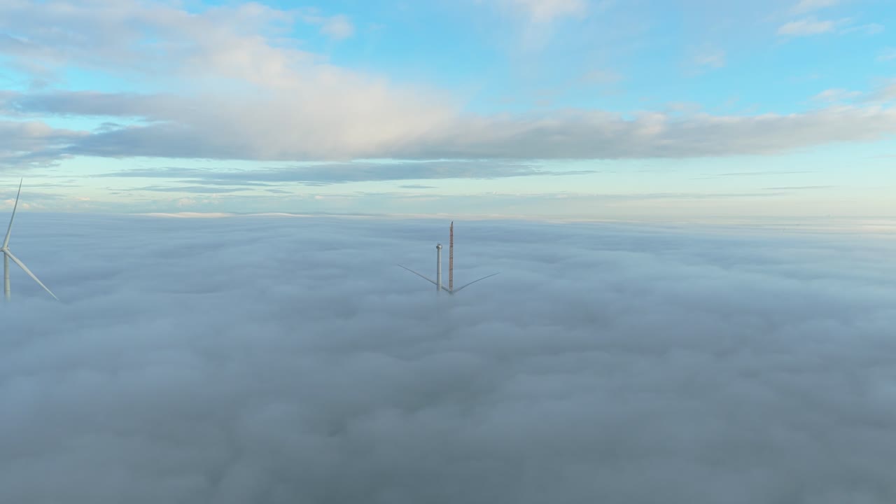 Crane lifts blades onto a partially built wind turbine in a misty scene