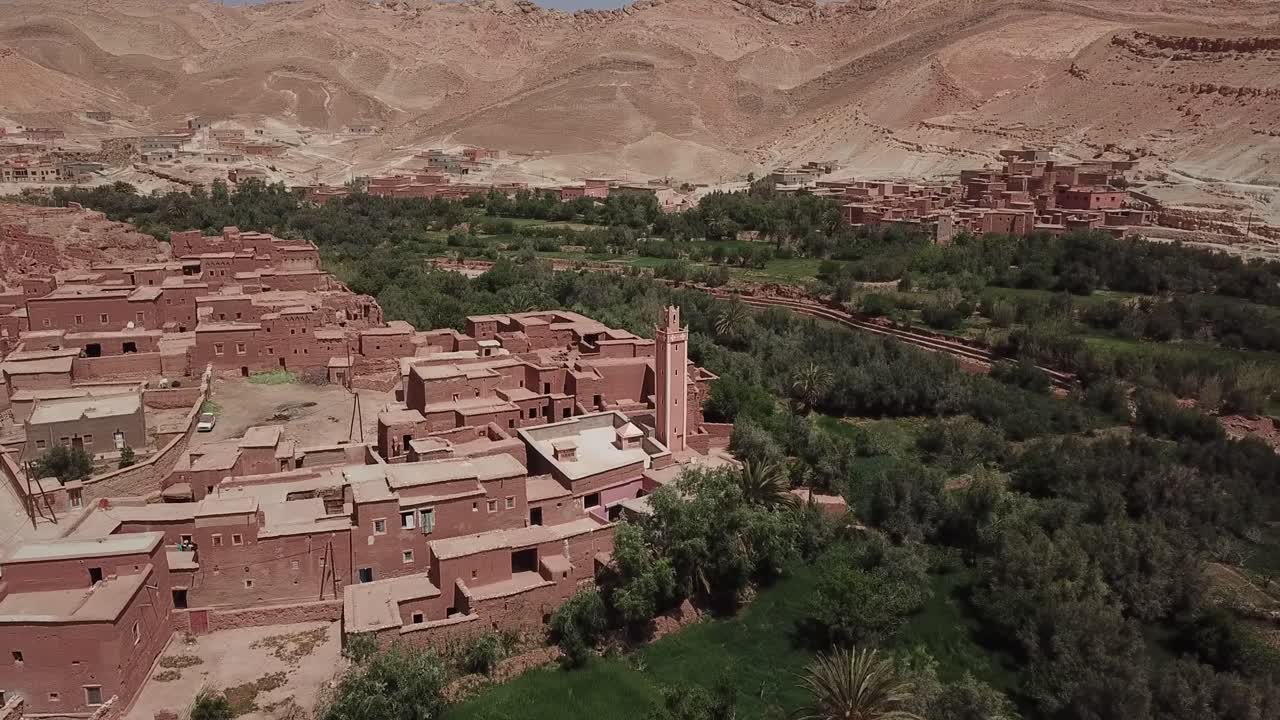 Veduta aerea con drone di un tradizionale villaggio nel deserto circondato da una lussureggiante vegetazione di oasi e palme a Ouarzazate. Forte contrasto tra l'insediamento e le colline aride, ideale per immagini di viaggio e culturali