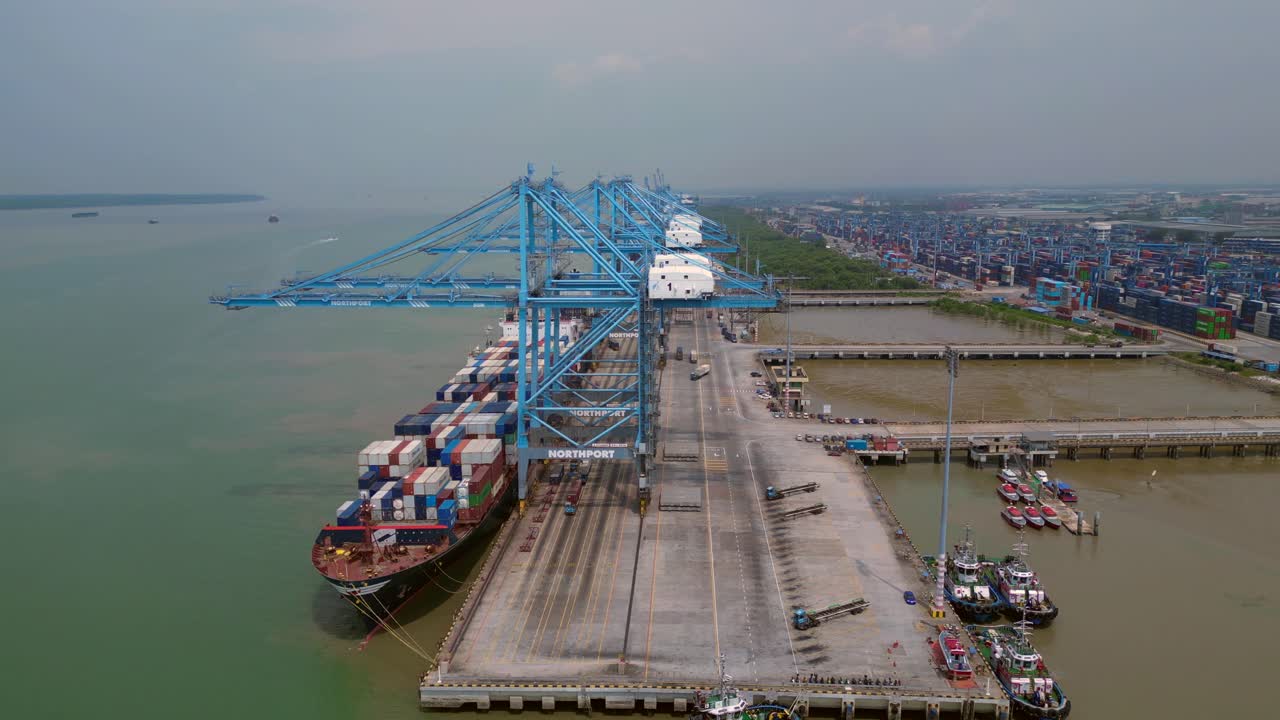 Container ship docked at a busy commercial port, cranes loading cargo containers. Global logistics and maritime trade infrastructure. Dramatic aerial view panorama overview drone