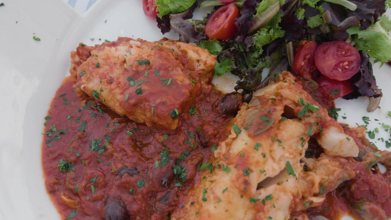 Primo piano di un filetto di pesce in salsa di pomodoro con olive accanto a un'insalata verde fresca