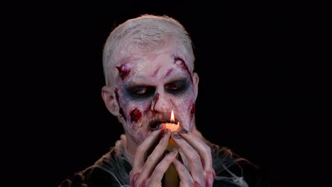 frightening man with halloween zombie bloody makeup spells conjures over candle, voodoo rituals