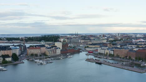 Panorámica-Aérea-Lenta-De-Barcos-A-Lo-Largo-De-La-Costa-Con-Una-Noria-A-La-Vista-Al-Atardecer,-Finlandia