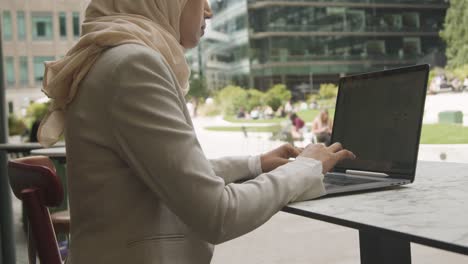 close up of muslim businesswoman sitting outdoors in city gardens working on laptop