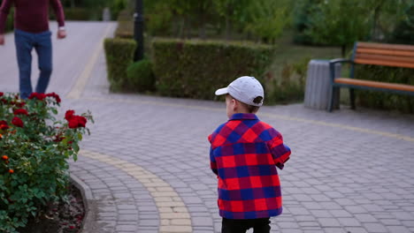 smiling baby boy in checkered shirt and cap runs around the flower bed. happy child runs up to his grandpa who picks him up. grandad and grandson in the park.