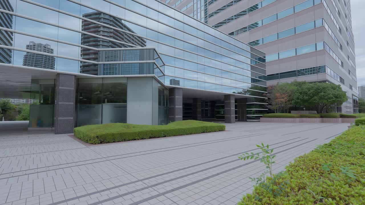 An eye-level shot of a modern glass office building exterior with manicured bushes and a paved walkway