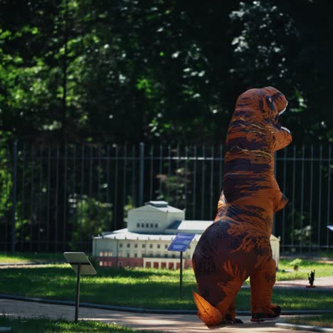 funny dragon outdoors. beautiful handmade buildings in the park and person in dragon suit walking nearby on green nature background.