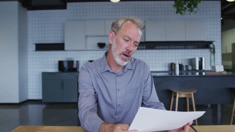 caucasian businessman having video chat going through paperwork in office kitchen