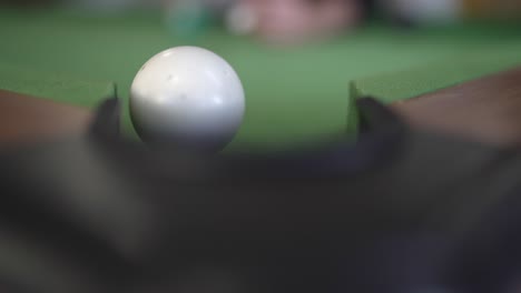 a close-up image captures the detail of a billiards table with a white cue ball striking and knocking another ball