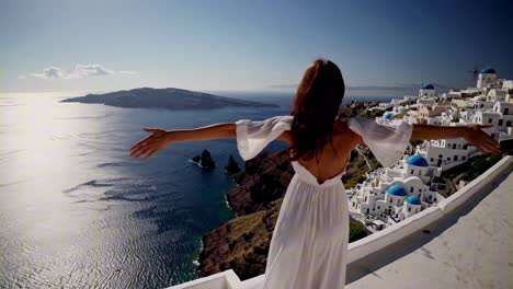 A woman in a white dress with arms outstretched overlooks a serene ocean view