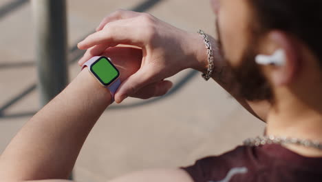 athletic man looking at left hand with smartwatch chroma key, touching interacts with green screen