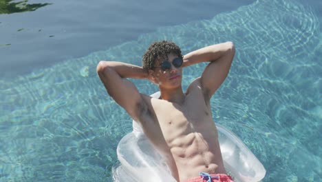 relaxed biracial man with sunglasses lying on inflatable in swimming pool on sunny day