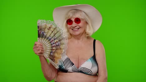 Senior-old-woman-tourist-exhales-from-heat-or-stuffiness,-waves-hand-fan-at-herself-on-chroma-key