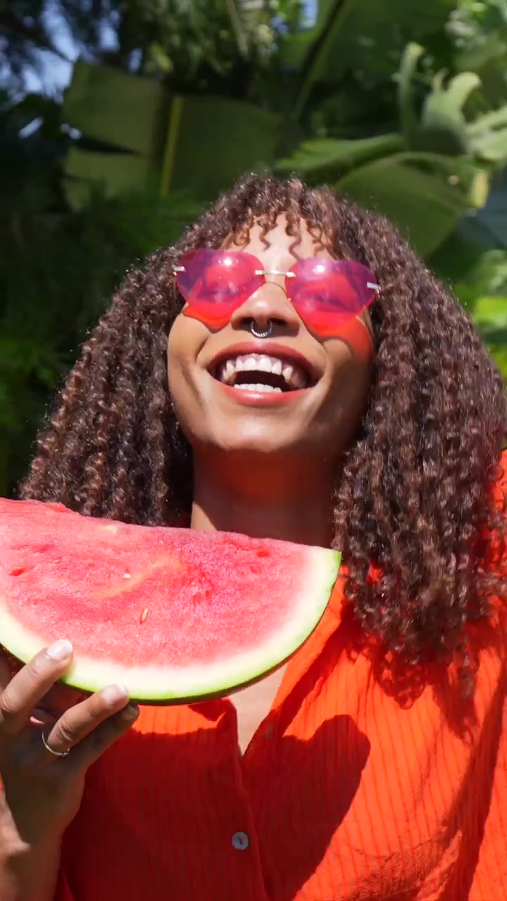 Mujer joven feliz con cabello rizado sonriendo y sosteniendo una sandía
