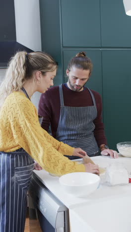 vertical video of diverse couple baking christmas cookies in kitchen at home, in slow motion