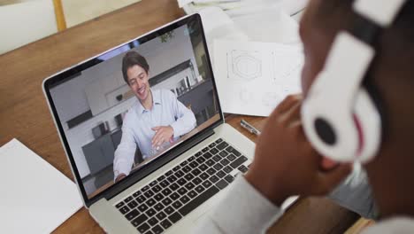 Afroamerikanischer-Geschäftsmann,-Der-Mit-Einem-Laptop-Am-Schreibtisch-Sitzt-Und-Einen-Videoanruf-Mit-Einem-Männlichen-Kollegen-Führt