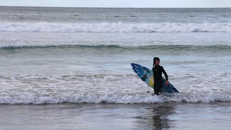 surfer walking out of the ocean with board