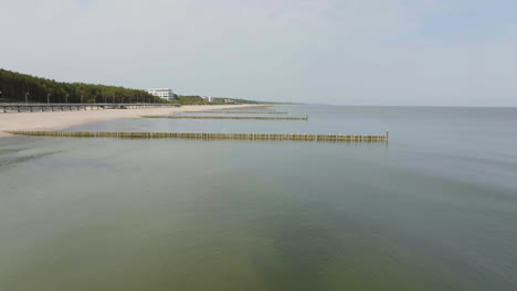 drone flying low over wavebreakers on a long beach, sunny day in mielno, poland