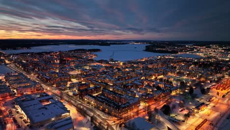 Ciudad-De-Luleå-Al-Atardecer-Con-Luces-De-La-Ciudad-Reflejándose-En-Calles-Nevadas-Y-Canales-Congelados,-Temporada-De-Invierno,-Vista-Aérea