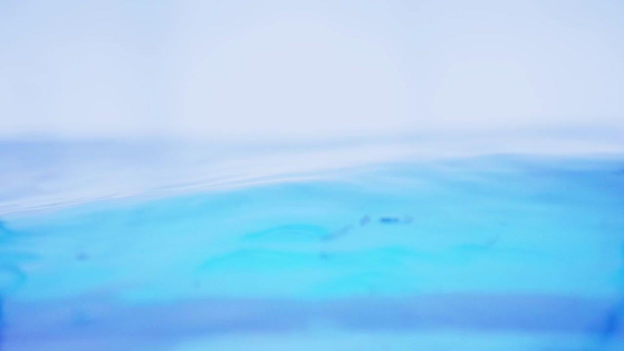 슬로우 모션의 깨끗한 물 표면은 물이 튀는 상점으로 화면을 채우고 기포로 액체 표면을 흔들고 있습니다.