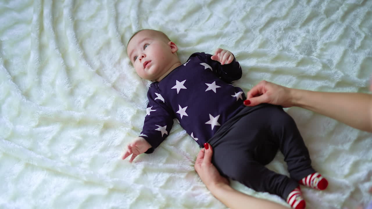 Little infant boy lying peacefully while mother putting pants on him. Adorable baby on the white backdrop. Top view.