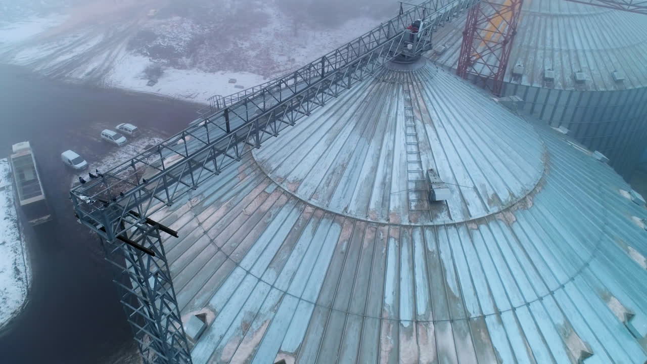 Grain storage containers from the tops on a misty winter day. Metal tanks towering over the dirty roads and cars. Aerial view.
