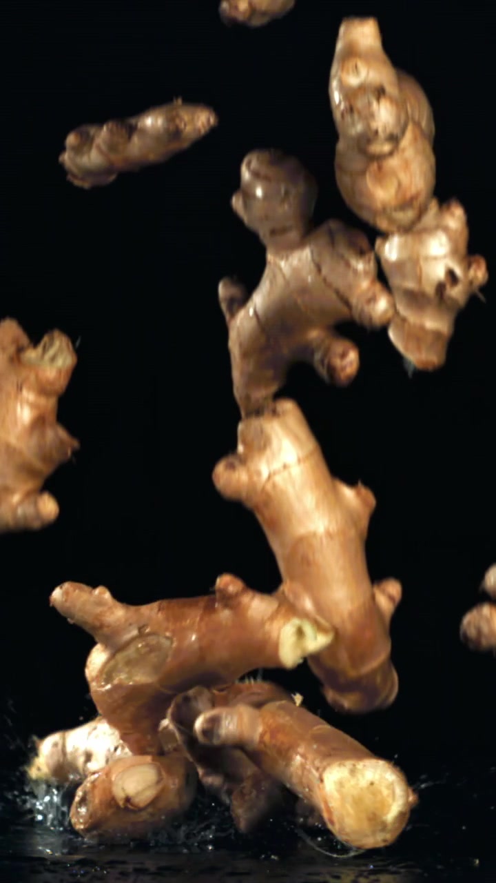 Fresh Ginger Roots Falling and Splashing on a Wet Black Surface in Slow Motion