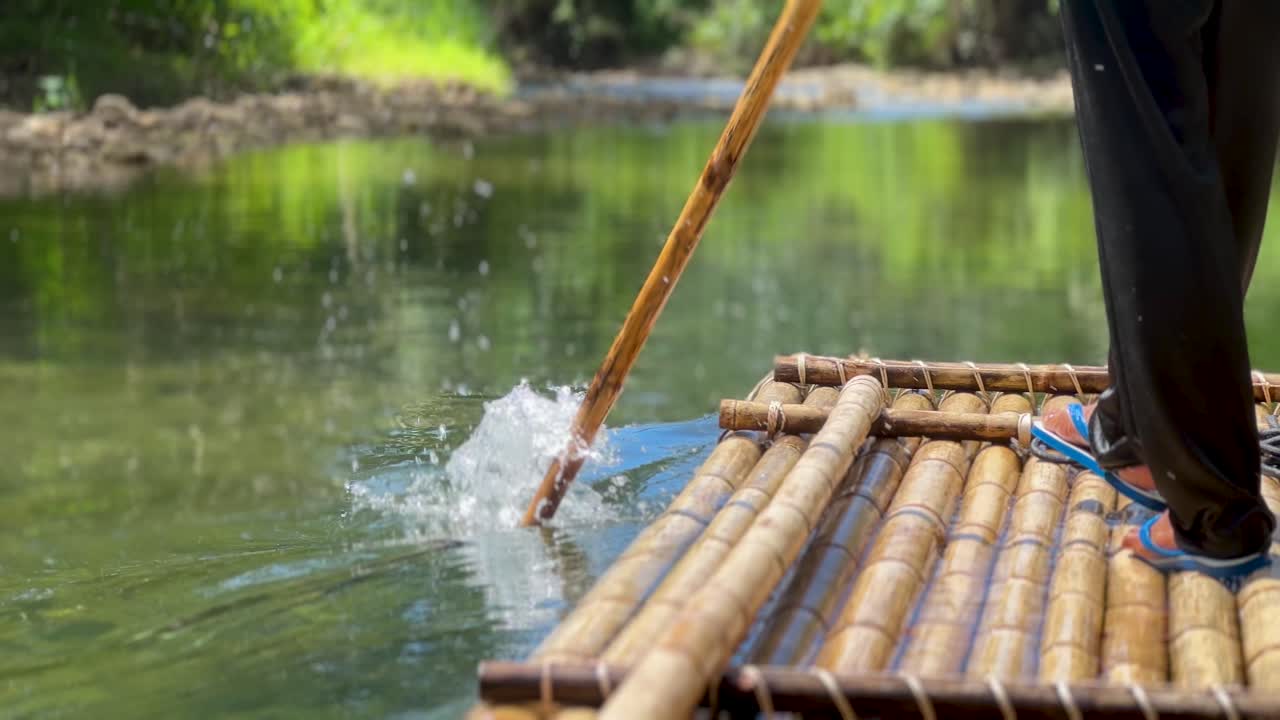 una persona tailandesa está usando un palo de bambú para dirigir una balsa de bambú por un río tranquilo en tailandia