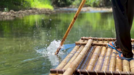 a thai person is using a bamboo stick to steer a bamboo raft down a calm river in thailand