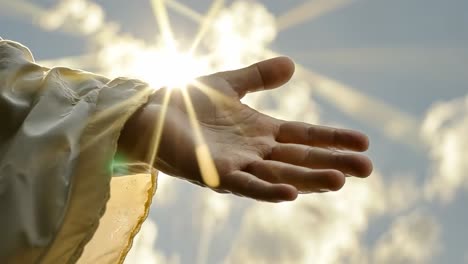 a hand reaching towards the sun with rays shining through clouds