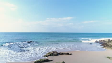 flying forward over a rocky sand beach towards the blue azure sea water in cadiz, spain