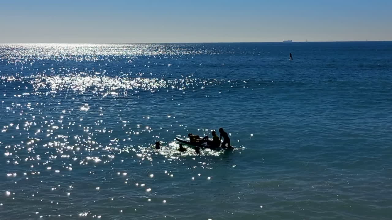 한 무리의 젊은이들이 패들 보드, 바다의 잔잔한 바다, 햇빛이 많이 반사되는 곳에서 즐거운 시간을 보냅니다.