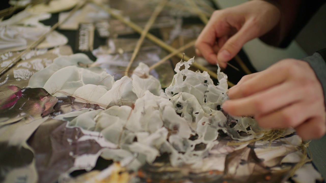 Primo piano di una mano che sistema materiali per una mood board di moda su un tavolo, inclusi bozzetti di capi stampati, campioni di tessuto e pezzi di plastica testurizzati.